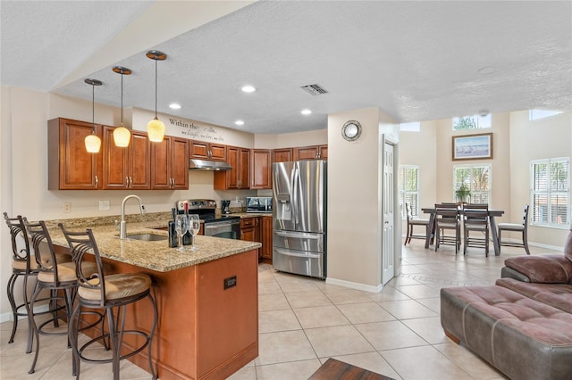 kitchen with light stone counters, light tile patterned floors, appliances with stainless steel finishes, a sink, and a peninsula