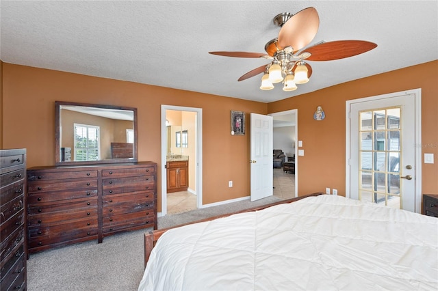 bedroom with a textured ceiling, light colored carpet, a ceiling fan, baseboards, and ensuite bath