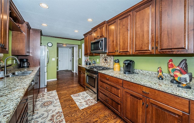 kitchen with appliances with stainless steel finishes, light stone counters, sink, and dark wood-type flooring