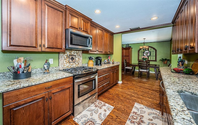 kitchen featuring dark wood-type flooring, light stone counters, decorative light fixtures, and appliances with stainless steel finishes