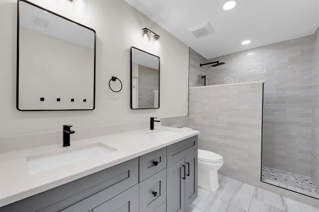 bathroom with vanity, toilet, tiled shower, and tile walls