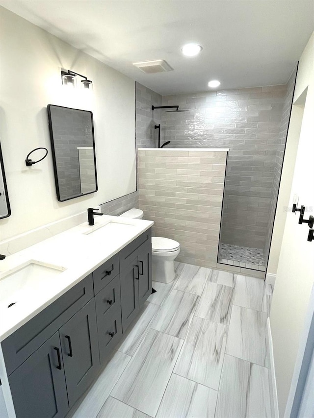 bathroom featuring a tile shower, vanity, toilet, and tile walls