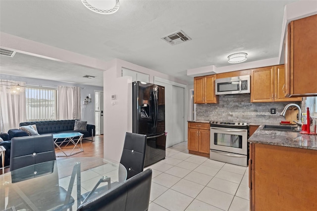 kitchen with light tile patterned floors, backsplash, appliances with stainless steel finishes, sink, and dark stone counters