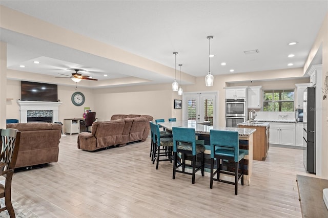 dining room featuring french doors, ceiling fan, a tray ceiling, and light hardwood / wood-style floors