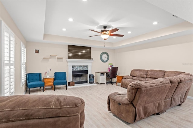 living room featuring light hardwood / wood-style floors, a raised ceiling, ceiling fan, and a fireplace