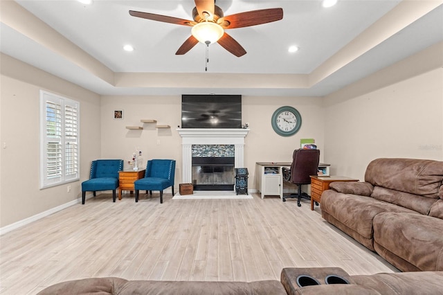 living room featuring light wood-type flooring, a raised ceiling, and ceiling fan