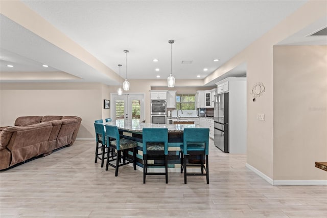 dining room with light wood-type flooring, french doors, a tray ceiling, and sink