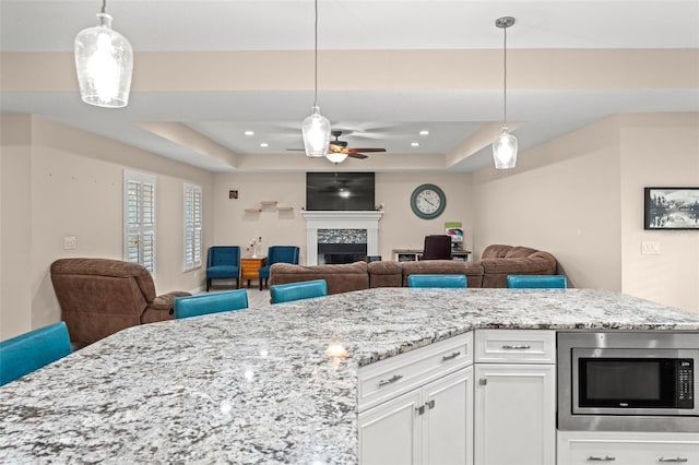 kitchen featuring decorative light fixtures, ceiling fan, a tray ceiling, stainless steel microwave, and white cabinets