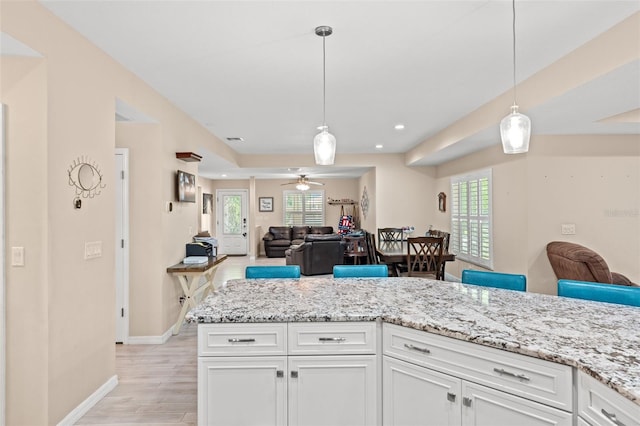 kitchen featuring light stone countertops, light hardwood / wood-style floors, hanging light fixtures, ceiling fan, and white cabinets