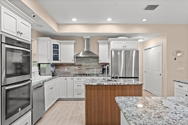 kitchen with appliances with stainless steel finishes, tasteful backsplash, light hardwood / wood-style floors, wall chimney range hood, and white cabinets