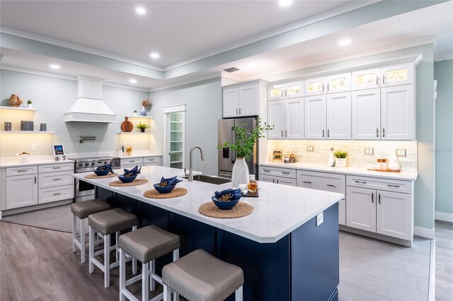 kitchen featuring white cabinetry, sink, stainless steel appliances, a kitchen island with sink, and custom exhaust hood