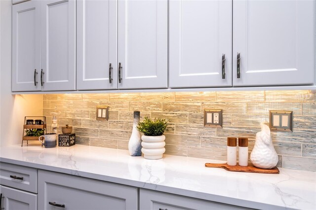 bar featuring backsplash, gray cabinets, and light stone countertops