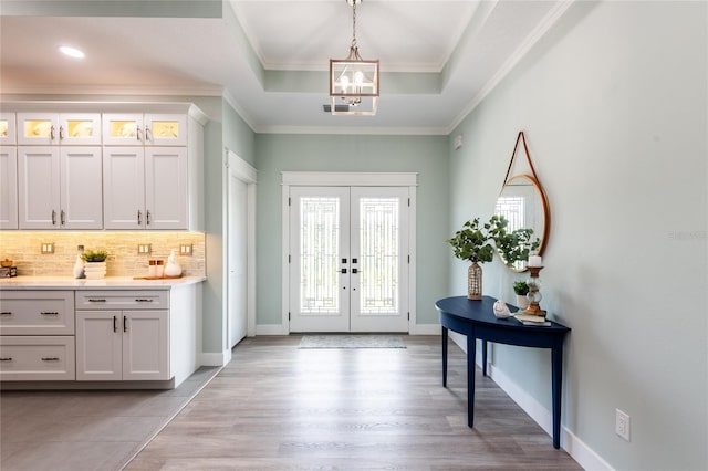 foyer featuring light wood finished floors, baseboards, ornamental molding, a tray ceiling, and french doors