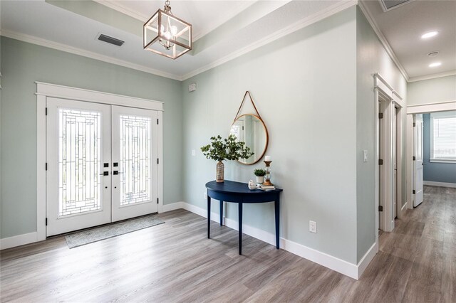 foyer with an inviting chandelier, light wood-type flooring, ornamental molding, and french doors