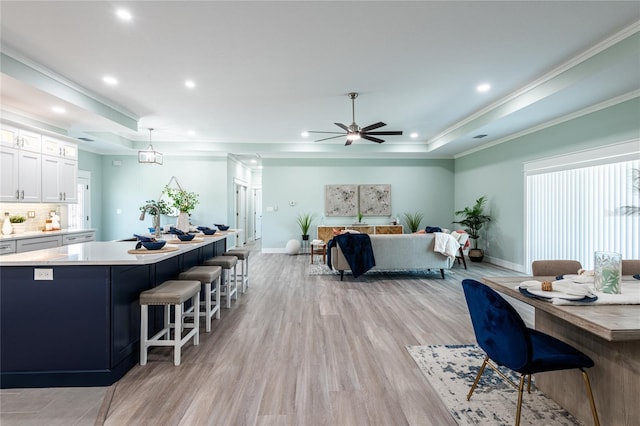 interior space with recessed lighting, a raised ceiling, light wood-style flooring, ornamental molding, and baseboards