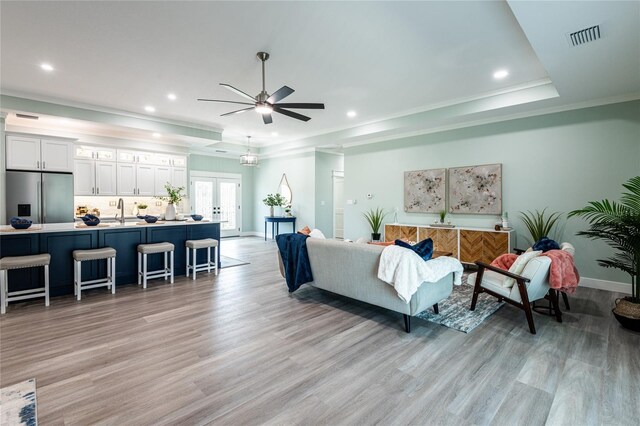 living room featuring french doors, ornamental molding, a tray ceiling, sink, and light hardwood / wood-style floors