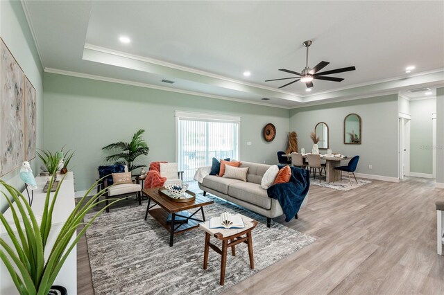 living room with a raised ceiling, crown molding, ceiling fan, and light wood-type flooring