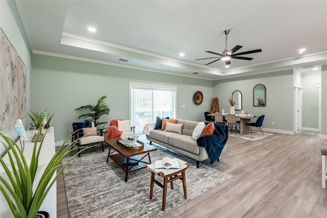 living area featuring baseboards, visible vents, a tray ceiling, crown molding, and light wood-type flooring