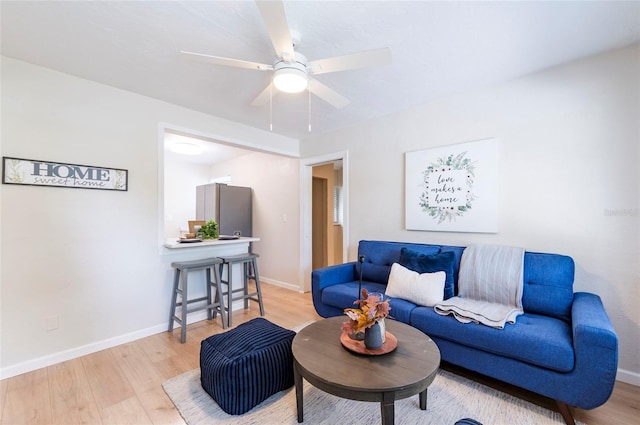 living room featuring light wood-style flooring, baseboards, and ceiling fan