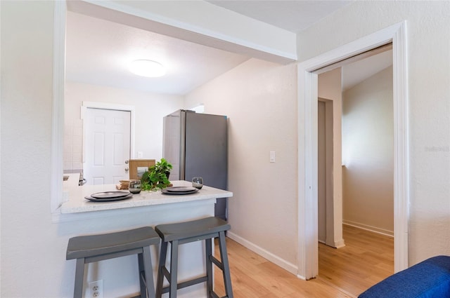 kitchen featuring light wood-type flooring, a breakfast bar, freestanding refrigerator, light countertops, and baseboards