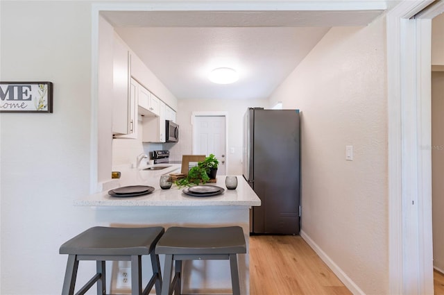 kitchen featuring a peninsula, stainless steel appliances, light countertops, white cabinets, and a kitchen breakfast bar