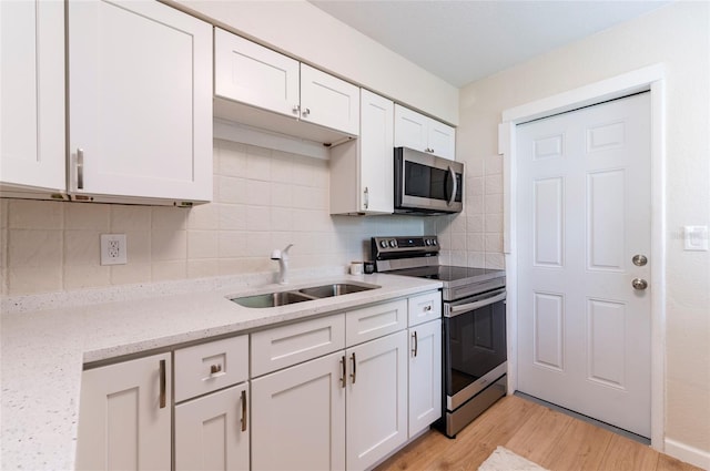 kitchen featuring a sink, backsplash, white cabinetry, stainless steel appliances, and light wood finished floors