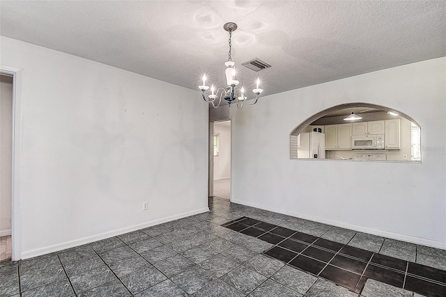 unfurnished room featuring a textured ceiling, an inviting chandelier, and dark tile patterned flooring