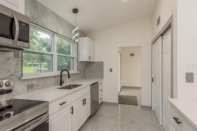 kitchen with pendant lighting, white cabinetry, sink, decorative backsplash, and appliances with stainless steel finishes