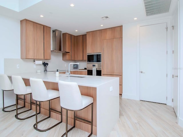 kitchen featuring a kitchen breakfast bar, light wood-type flooring, wall chimney exhaust hood, and stainless steel oven