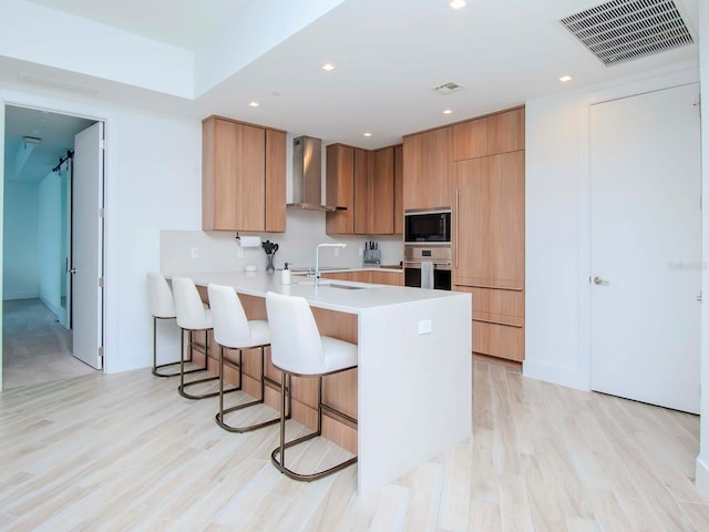 kitchen featuring light hardwood / wood-style floors, wall chimney range hood, black microwave, and stainless steel oven