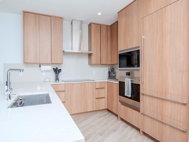 kitchen with light brown cabinets, wall chimney exhaust hood, light hardwood / wood-style floors, sink, and stainless steel appliances