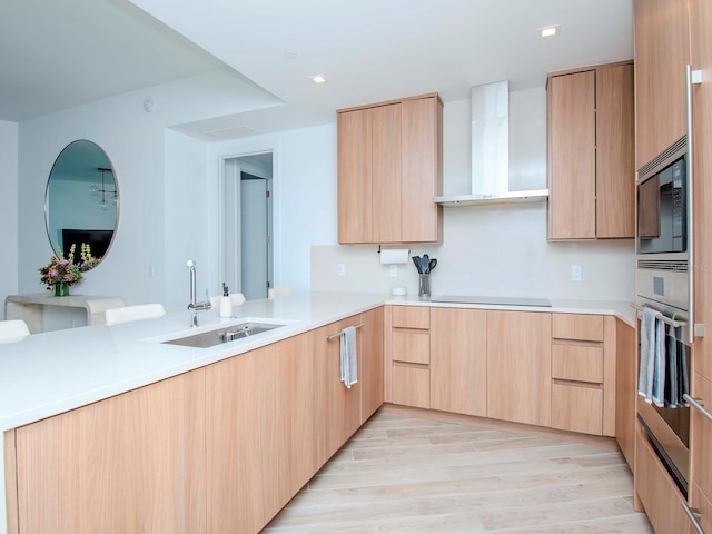 kitchen featuring stainless steel appliances, wall chimney exhaust hood, sink, light brown cabinets, and light wood-type flooring