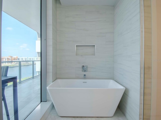 bathroom featuring a bathing tub, a water view, tile patterned flooring, and tile walls