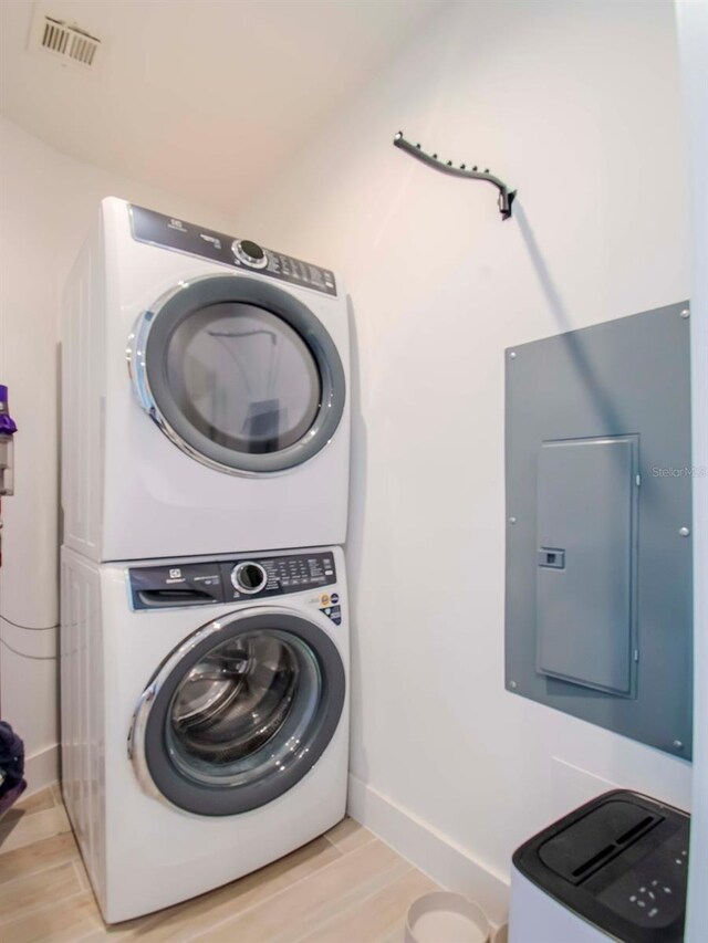 laundry room featuring stacked washer / dryer, light hardwood / wood-style flooring, and electric panel