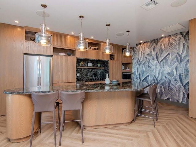 bar with decorative light fixtures, light parquet flooring, dark stone countertops, and stainless steel refrigerator