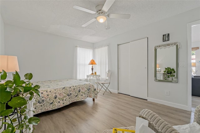 bedroom with ceiling fan, a closet, light hardwood / wood-style floors, and a textured ceiling