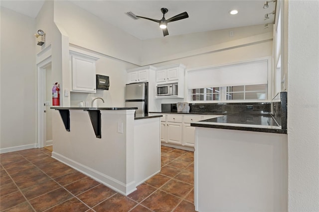 kitchen with appliances with stainless steel finishes, white cabinets, ceiling fan, and kitchen peninsula