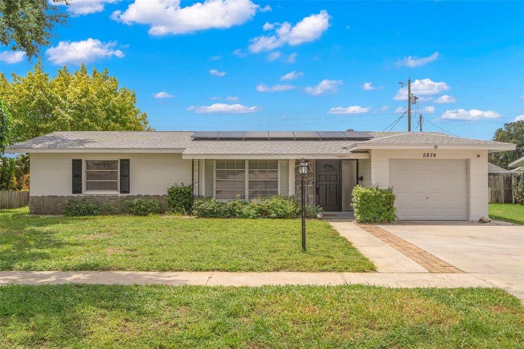 ranch-style house with solar panels, a garage, and a front yard