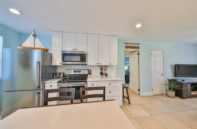 kitchen with tasteful backsplash, white cabinets, light tile patterned flooring, and appliances with stainless steel finishes