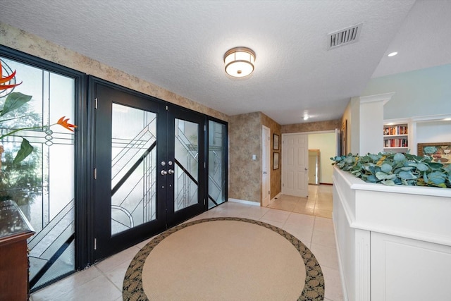 foyer entrance with a textured ceiling, light tile patterned floors, and french doors