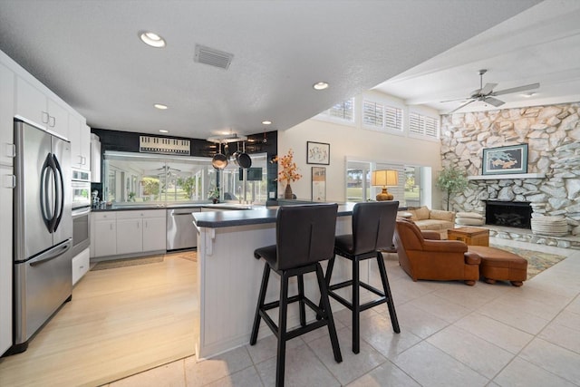 kitchen featuring a stone fireplace, light wood-type flooring, ceiling fan, white cabinetry, and stainless steel appliances