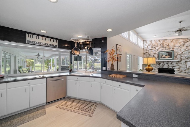 kitchen with dishwasher, light hardwood / wood-style floors, white cabinetry, ceiling fan, and a stone fireplace