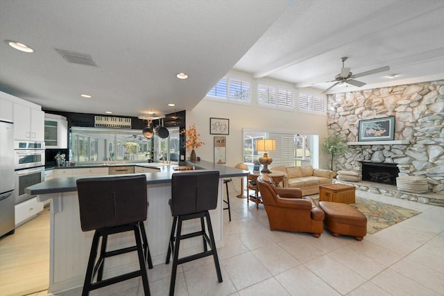 kitchen featuring a breakfast bar, a fireplace, light wood-type flooring, ceiling fan, and white cabinets