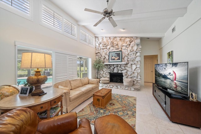 tiled living room featuring ceiling fan, beamed ceiling, a high ceiling, and a stone fireplace