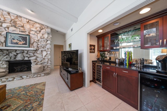 bar featuring beverage cooler, a stone fireplace, and light tile patterned floors