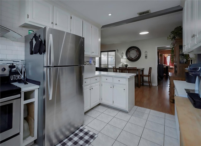 kitchen with stainless steel refrigerator, kitchen peninsula, light tile patterned floors, white cabinets, and white electric range