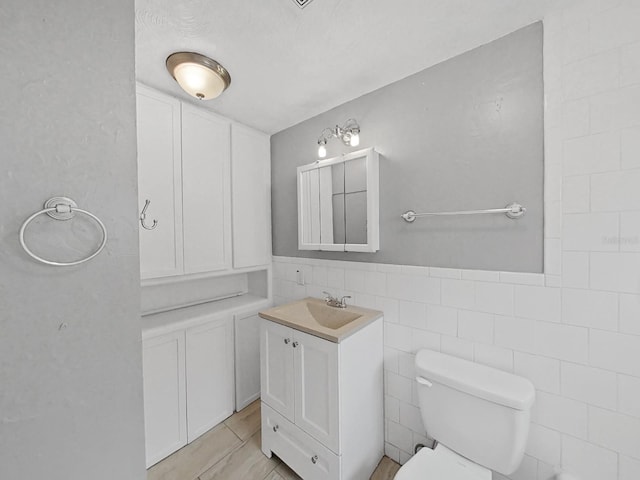 bathroom with tile walls, toilet, vanity, and tile patterned floors