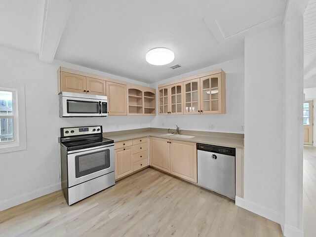 kitchen with sink, light wood-type flooring, appliances with stainless steel finishes, beamed ceiling, and light brown cabinets