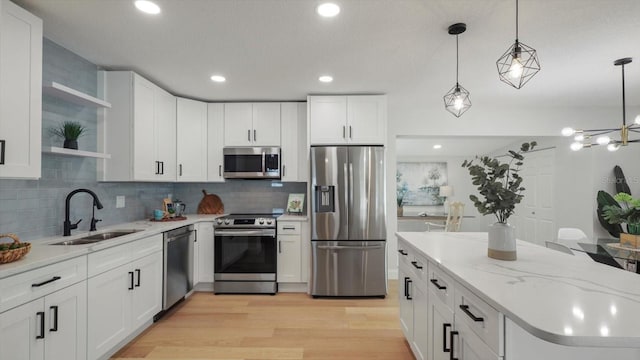 kitchen with appliances with stainless steel finishes, decorative backsplash, white cabinetry, sink, and light wood-type flooring