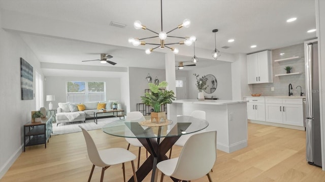 dining area featuring ceiling fan with notable chandelier, sink, and light hardwood / wood-style flooring